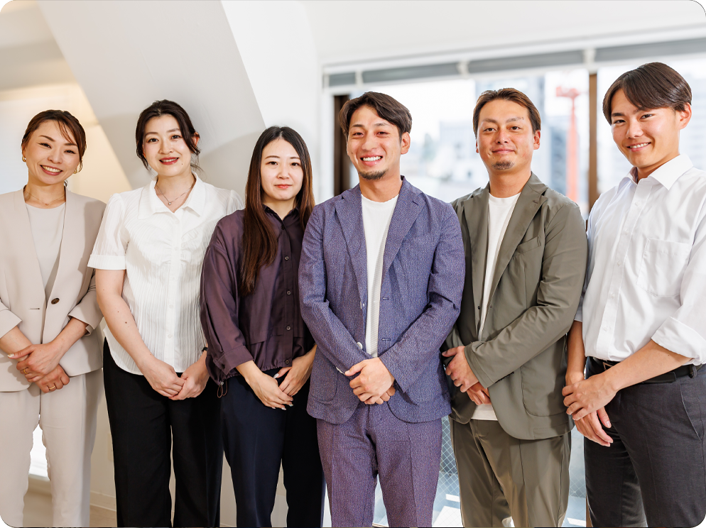 工場を背景に笑顔で並ぶ多様な社員たち
